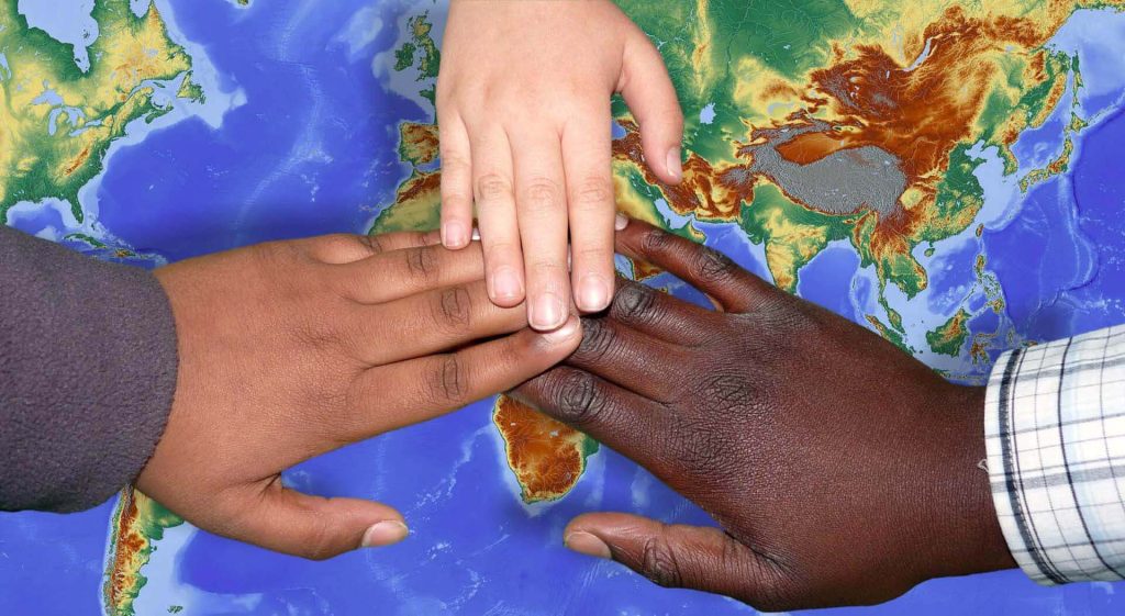 Black, brown and white hands touching each other and a world map